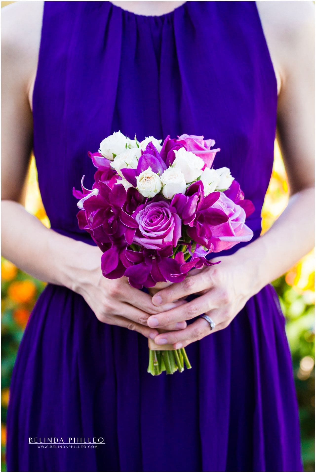 Bridesmaid wearing purple gown shows off her white and purple bridesmaid bouquet made of roses and orchids at Friendly Hills Country Club Wedding
