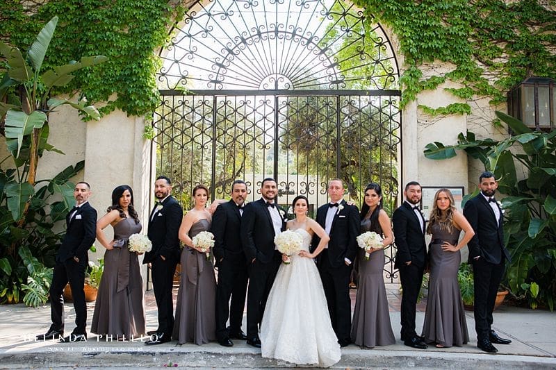 Bridal party poses in front of stunning gate at Los Angeles River Center & Gardens. Bride's gown is Martina Liana in Carmen + Sander style. Bridesmaids wearing White by Vera Wang v-wire crepe mermaid in Charcoal