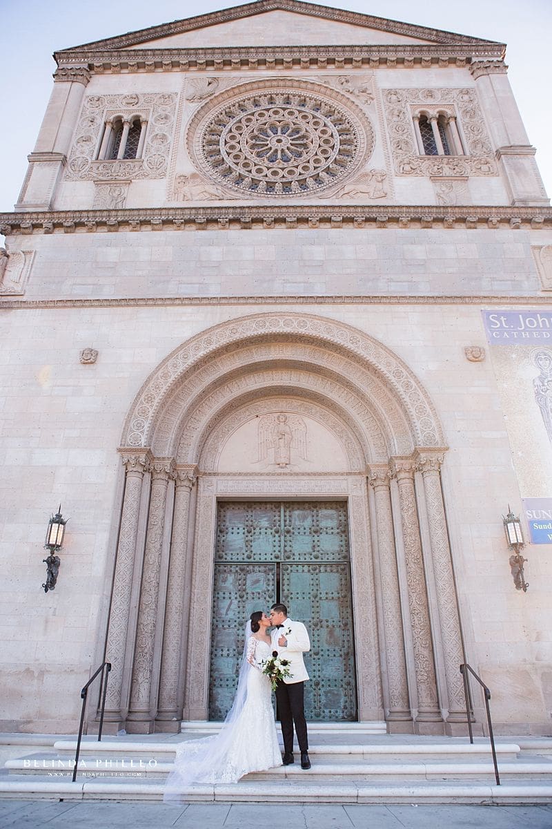 Bride and groom share a kiss on the front steps of St John's Cathedral in Los Angeles, CA. Photography by Belinda Philleo