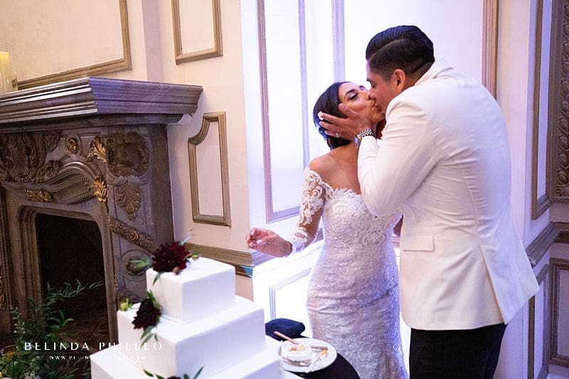Newlyweds share a kiss after cutting their cake during their wedding at Alexandria Ballrooms, Los Angeles, Ca. Photography by Belinda Philleo