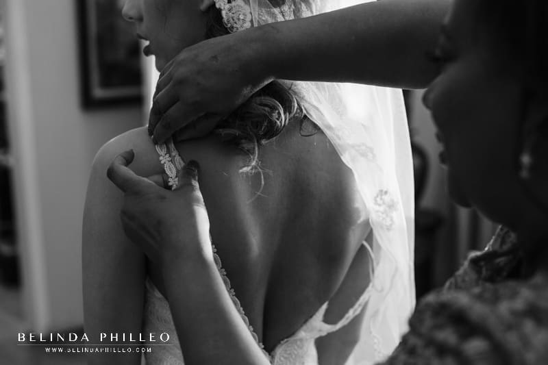 Bride's mother helps her put on her Justin Alexander wedding gown