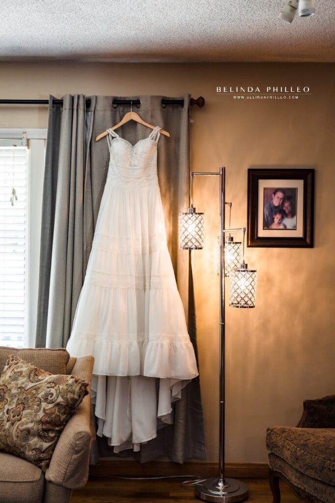 Justin Alexander bohemian style wedding gown hangs in bride's living room while she gets ready.