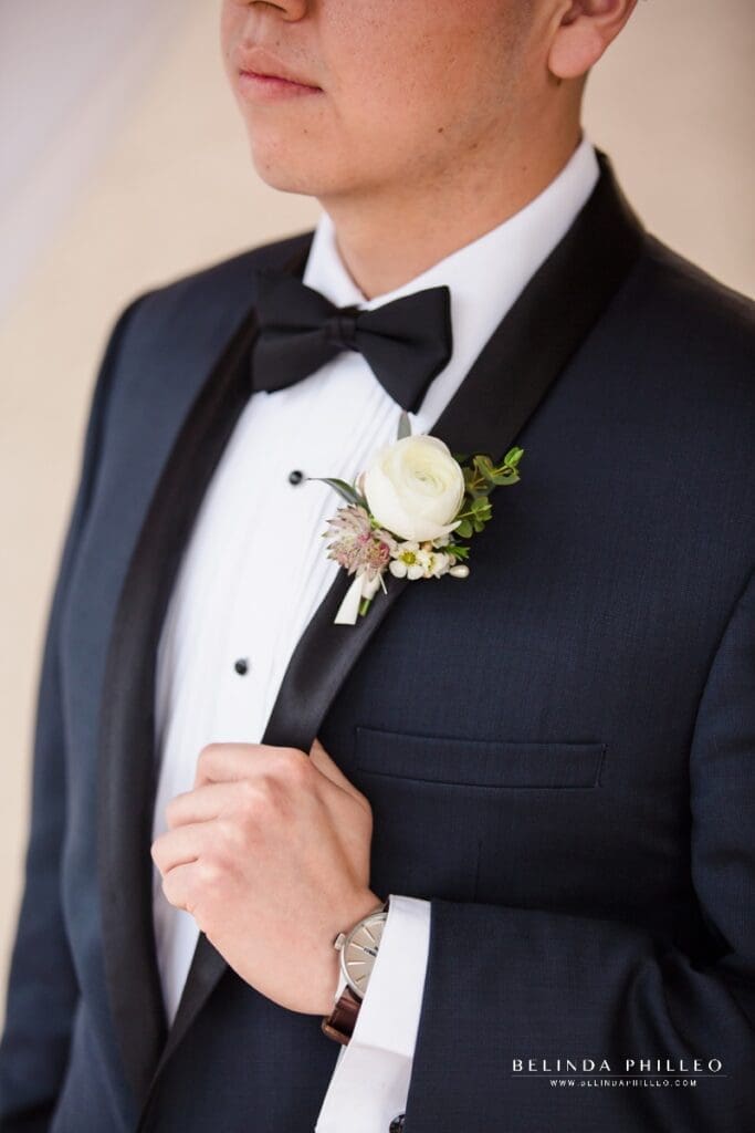 Groom in a navy tux with black lapel and white ranunculus boutonniere