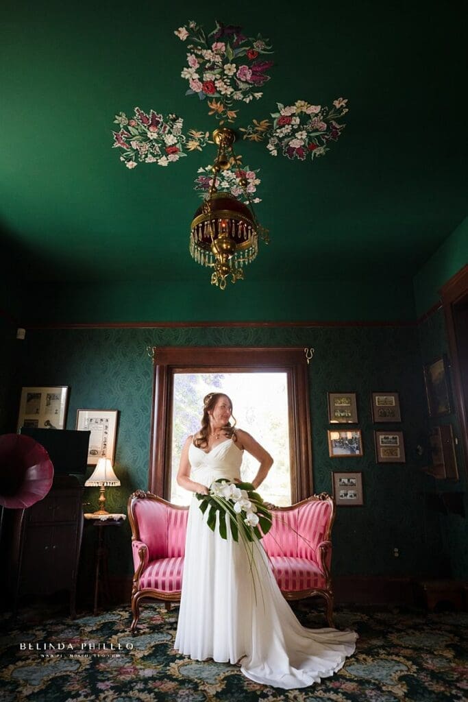 Bride shows off her simple bridal gown with spaghetti straps from David's Bridal and her tropical floral arrangement. Taken at Heritage Museum of Orange County wedding. Photo by Belinda Philleo