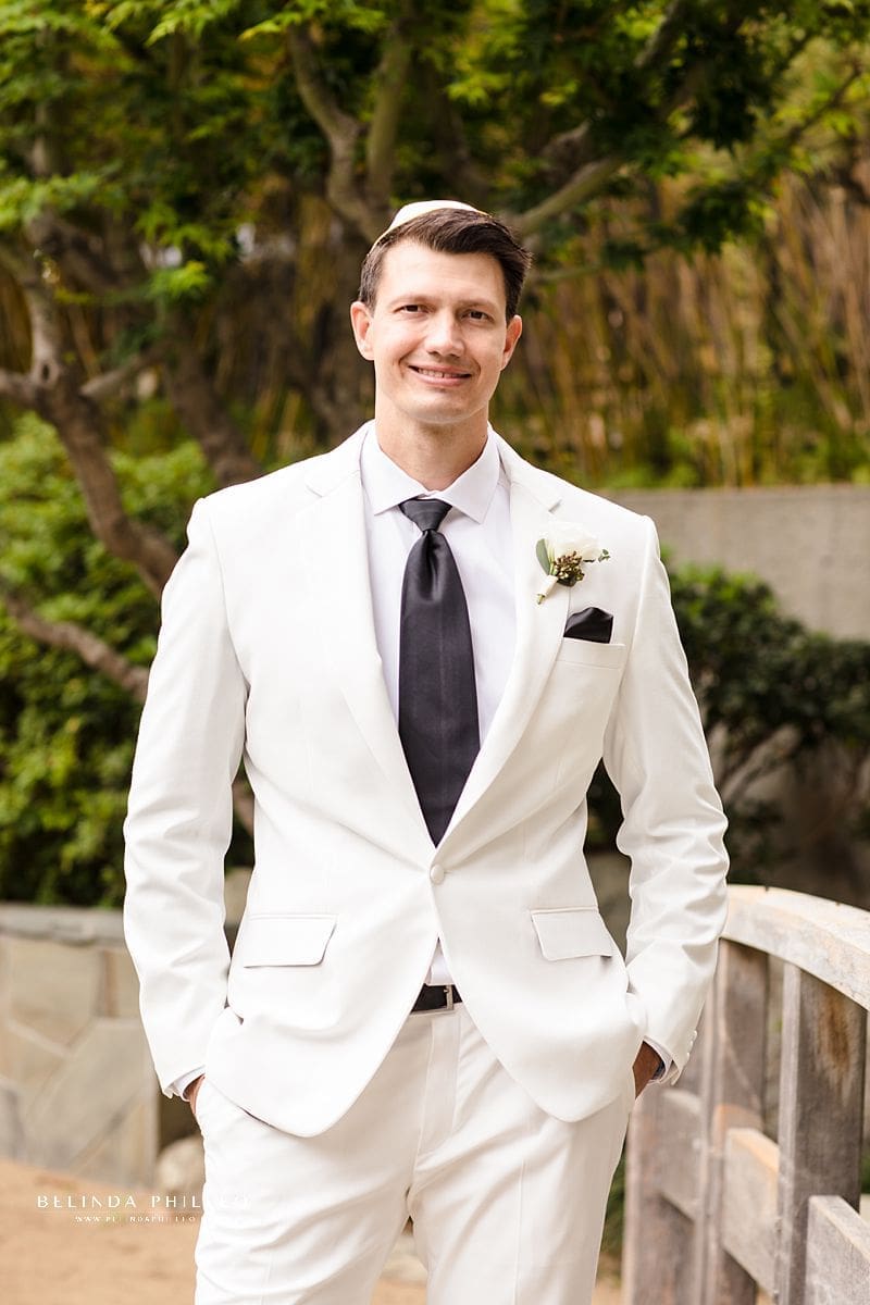 Groom shows off is white custom suit before wedding ceremony in the garden at JACCC in Los Angeles, CA