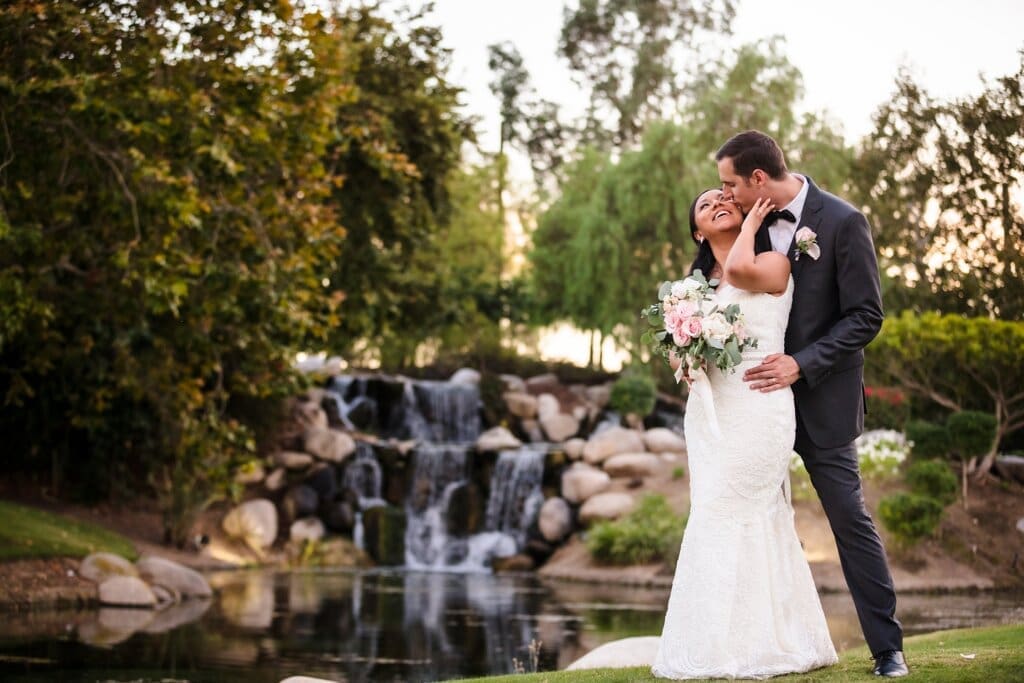 Newlyweds share a kiss in front of waterfall at Coyote Hills Golf Course wedding in Fullerton, CA. Photography by Belinda Philleo