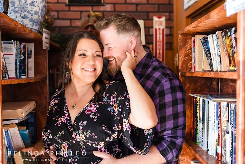 An engaged couple flirt as they browse books in a coffee shop library