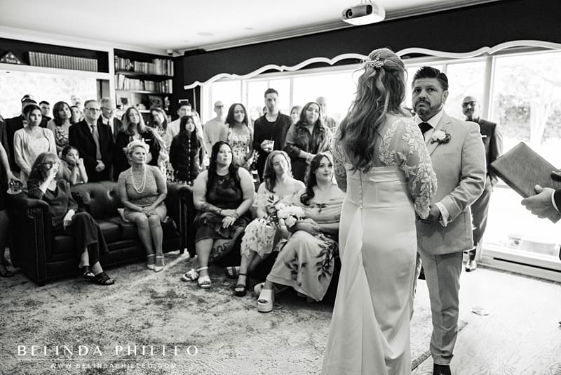 Black and white image of a couple getting married in their living room as a small crowd looks on
