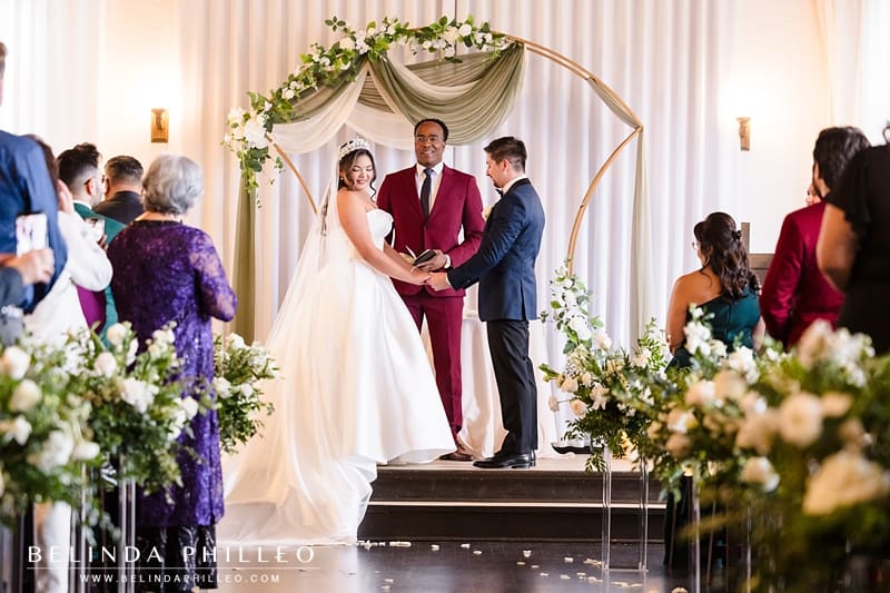 Bride and groom hold hands during their wedding ceremony and guests look on